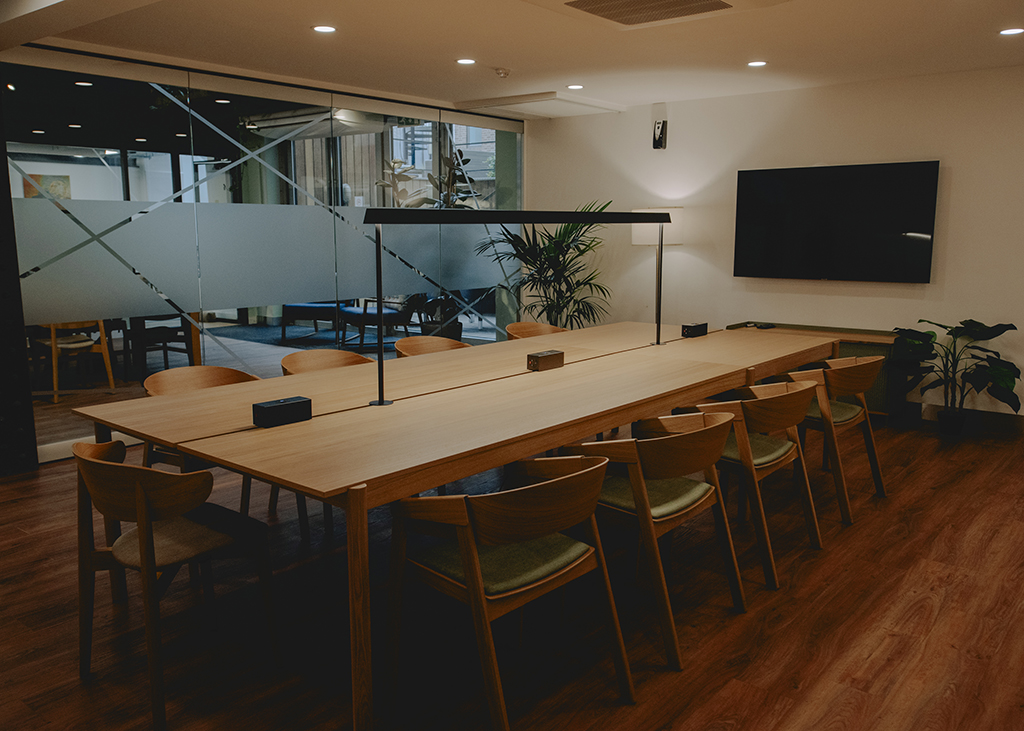 A beautiful large meeting room with a boardroom table, a full glass door, lovely lighting and a screen.